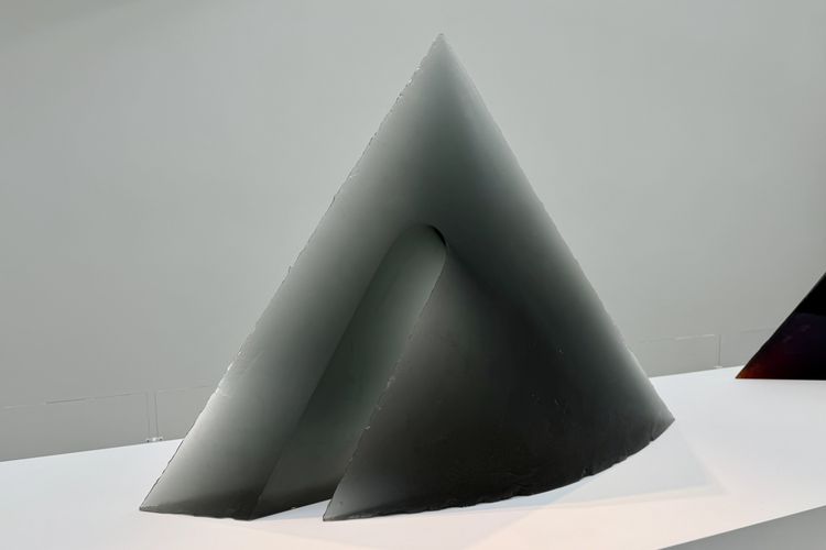A large, translucent dark gray cast glass sculpture titled 